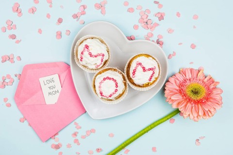 Muffins with mom word plate near flower envelope with tag confetti