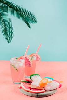 Palm leaves grapefruit cocktail glasses popsicles coral desk against teal background