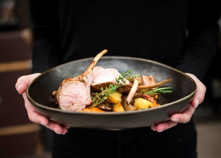 Person holding lamb ribs dish