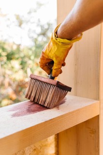 Person varnishing piece wood from house construction