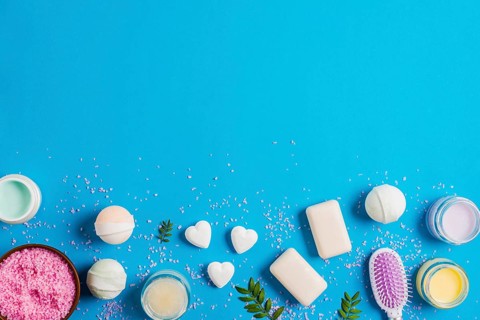 Pink salt bowl bath bomb soap hairbrush moisturizer cream blue background