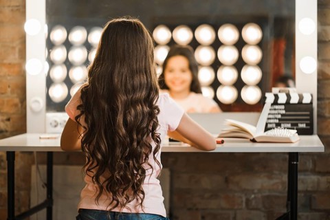Rear view girl with long brunette wavy hair sitting makeup room