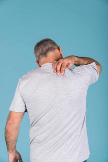 Rear view man suffering from neck pain front blue backdrop
