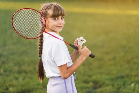 Smiling girl holding badminton her shoulder shuttlecock