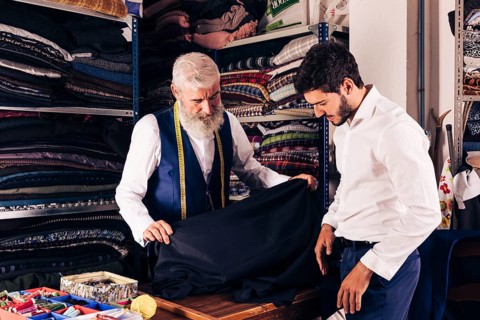 Smiling man seller displaying blue fabrics young customer textile shop