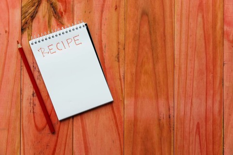 Spiral notepad near recipe word near pencil wooden background