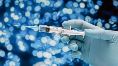 Syringe with vaccine held by hand with glove