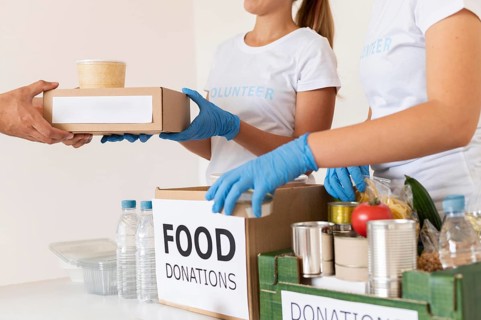 Volunteers with gloves handing boxes with food donation