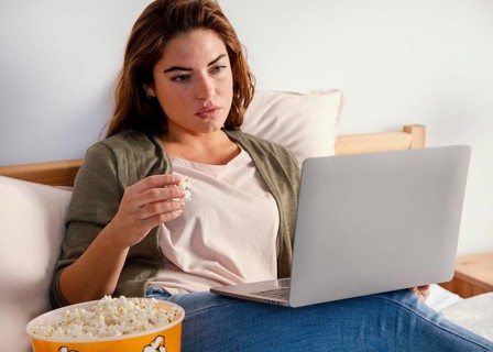 Woman eating popcorn while watching movie laptop