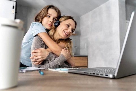 Woman with headset working laptop hugged by girl