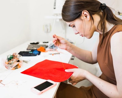 Young woman sewing red cloth with needle