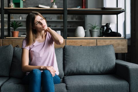 Young woman sitting sofa having neck pain