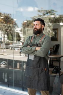 Bearded serious hairdresser standing outside near barbershop