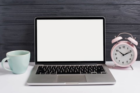 Ceramics cup alarm clock open laptop white desk against wooden black background