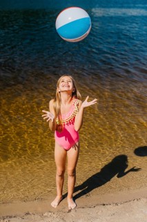Cheerful girl throwing beach ball standing against sea