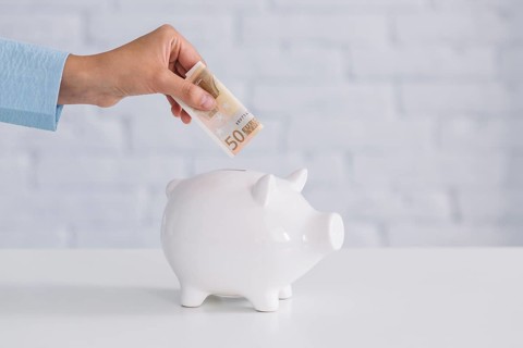 Close up person s hand inserting fifty euro banknote piggybank desk