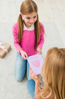 Cute daughter giving greeting card mother