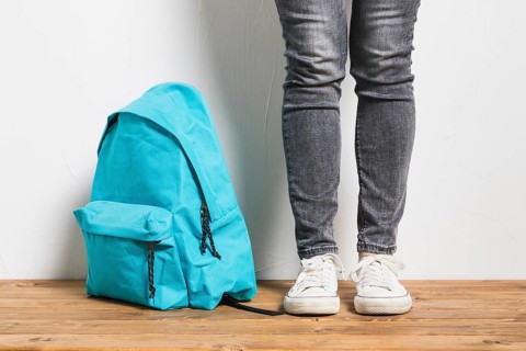 Faceless person standing beside schoolbag wooden table