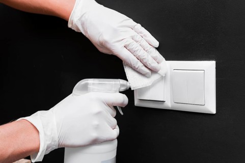 Hands with gloves disinfecting light switches
