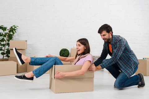 Husband pushing his wife sitting cardboard box