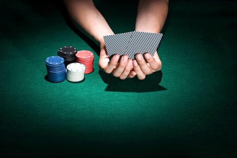 Person hand holding playing card with stacking poker chips casino table