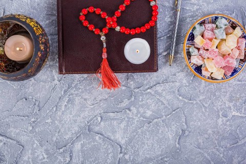 Red prayer beads candle diary pen lighted candle with bowl rakhat lukum rough grey textured background