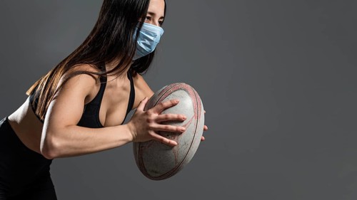 Side view athletic female rugby player holding ball while wearing medical mask