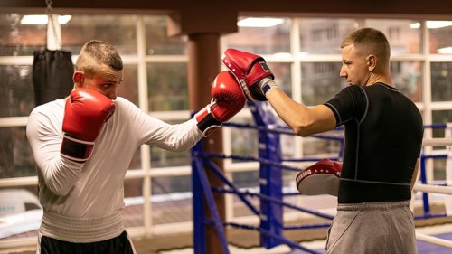 Side view male boxer practicing with trainer ring