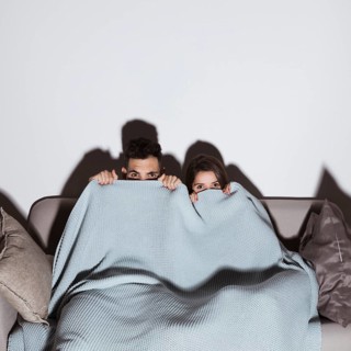 Woman man coverlet watching tv sofa dark room