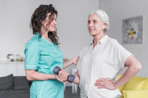 Beautiful old lady is doing exercise with dumbbell with help physiotherapist