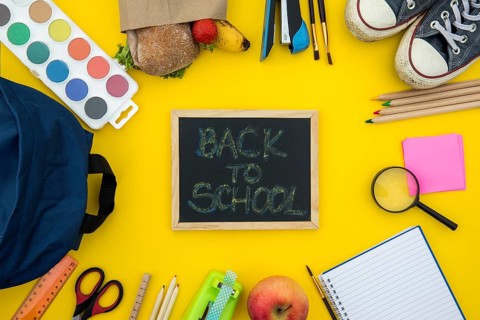 Blackboard with school accessories yellow background