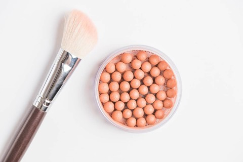 Bronzing pearls with makeup brush white background