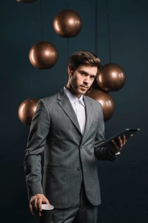 Confident young man holding disposable cup digital tablet against dark background
