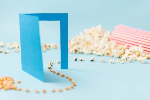 Corn seeds going through blue paper doorway turning into popcorn blue backdrop