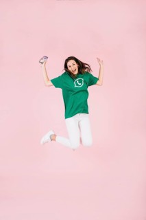 Excited woman with cellphone jumping pink background