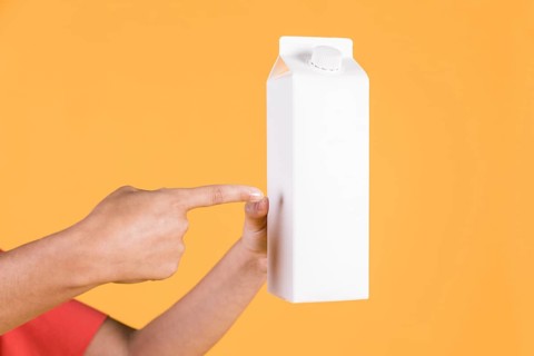 Female pointing finger white tetra pack against yellow backdrop
