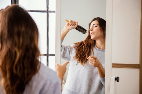 Front view happy woman singing into hairbrush home