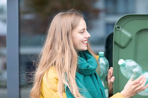 Young woman with plastic bottles at a green rubbish bin as environmental protection