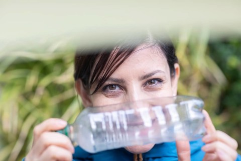 Woman with a plastic bottle in front of a wall of plants Environmental protection