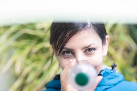 Woman with a plastic bottle in front of a wall of plants Environmental protection