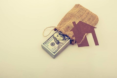 Paper house placed beside a bundle of US dollar banknote