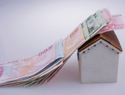 Turkish Lira banknotes on the roof of a model house on white background