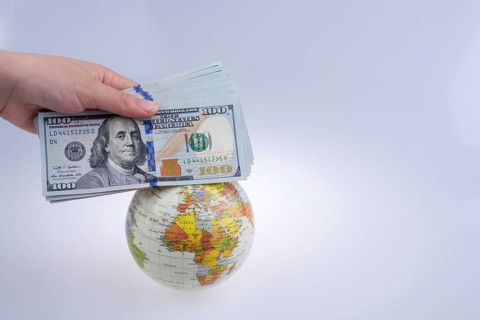 Human hand holding American dollar banknotes by the side of a model globe on white background