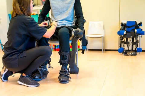 Mechanical exoskeleton. Physiotherapy in a modern hospital: Female physiotherapist helping disabled person with robotic skeleton with tapes. Futuristic rehabilitation