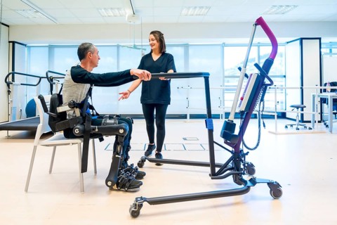 Mechanical exoskeleton. Physiotherapy assistant lifting disabled person with robotic skeleton to get up. Futuristic rehabilitation