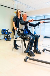 Mechanical exoskeleton. Female physiotherapy doctor assistant lifting disabled person with robotic skeleton to get up. Futuristic rehabilitation
