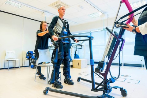 Mechanical exoskeleton. Female physiotherapy medical assistant lifting disabled person with robotic skeleton. Futuristic rehabilitation