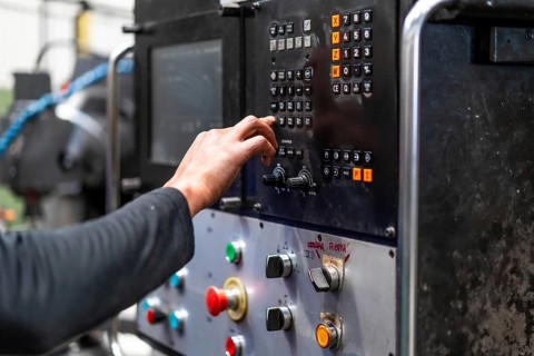 Unrecognizable operator touching the panel of a numerically controlled metal industrial factory machine