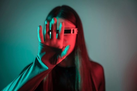 Futuristic studio portrait with neon lights of a transgender person gesturing while using augmented reality smart goggles