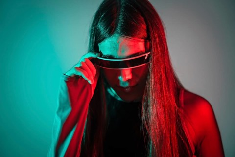 Studio portrait with neon lights of a curious futuristic transgender person using smart goggles